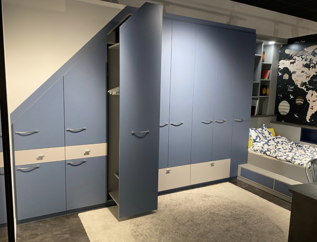 Chambre d’enfant sur-mesure avec placard sous pente, armoires bleues, lit intégré et bibliothèque, conçue par Louarn Intérieurs à Lorient